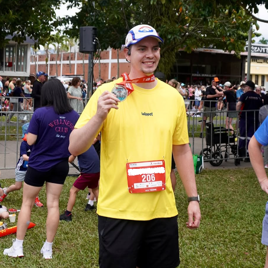 Man in Wippet Blazing Yellow Everyday Running Shirt that is breathable, sun protection and sweat wicking with race bib holding a medal at an outdoor event.